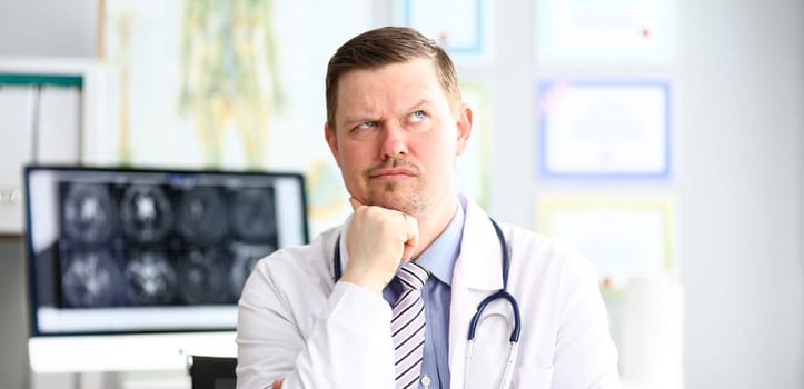Male doctor with strange facial expression sit in his office headshot