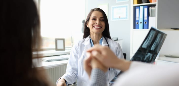Portrait of smiling doctor holding x-ray and reporting good news to patients. Happy woman looking at couple with gladness. Healthcare and treatment concept