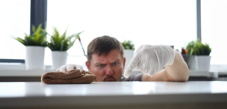 Focus on gloved hand of diligent male touching white office workplace and holding brown loincloth and swiping dust with harmful germs. Pleasant clean-up concept. Blurred background