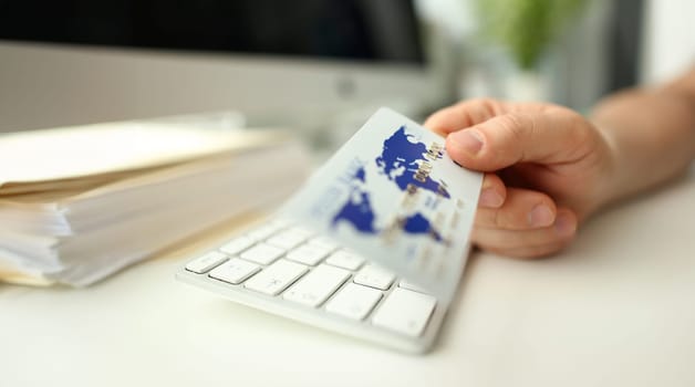 Male hand hold plastic bank card aganist keyboard background. Fast money transaction concept.
