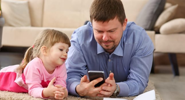 Father and daughter lie on floor using mobile phone portrait