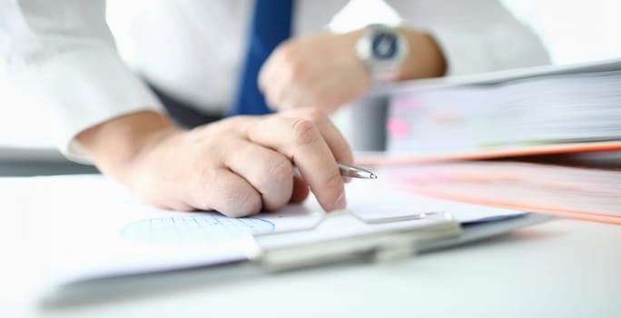 Focus on male hand with golden wedding ring holding ball pen. Man in office reading conditions of profitable contract. Business concept. Blurred background