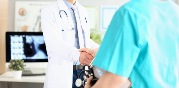 Two doctors in office shaking hands celebrating successful treatment closeup