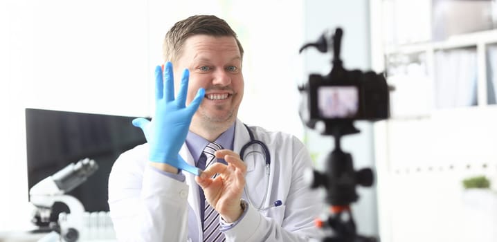 Funny smiling doctor demonstrative pulling on protective gloves on arm ready to give some medical advices to his subscribers portrait concept