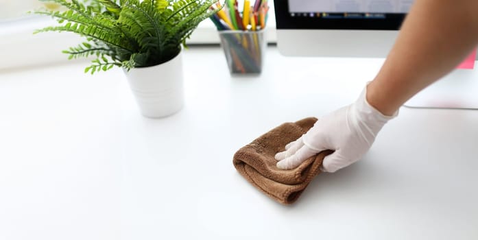Focus on gloved male hand holding cloth and swiping all dirt and dust inhabited by harmful bacteria from white office table with concentration and diligence. Pleasant clean-up concept