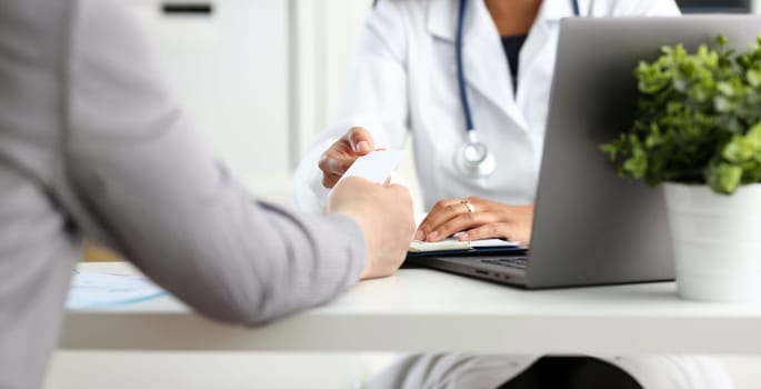 Female physician hand give white blank calling card to businesswoman closeup in office. Physical disease prevention examine patient instrument shop healthy lifestyle family doctor concept