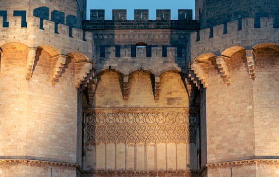 Close-up of the Serranos Towers in Valencia, Spain, illuminated at night. The detailed architectural features and lighting create a historic and majestic atmosphere.