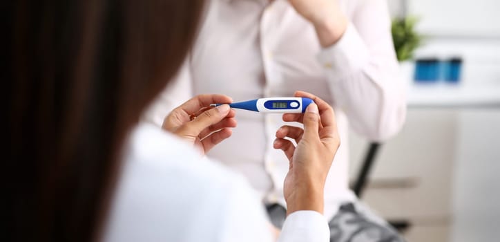hands of a female doctor holding a thermometer with a patient's high temperature in hand