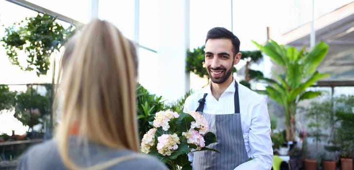Smiling italian man seller of flowers stretches finished bouquet to woman. Small business holiday decoration concept.
