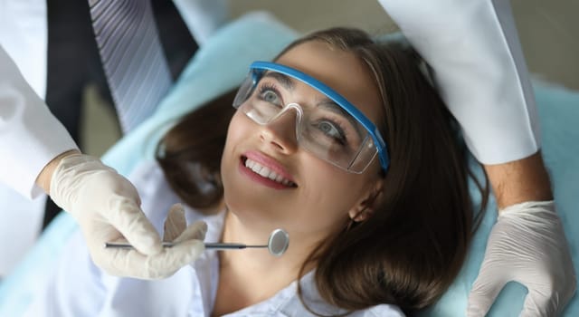 Close-up of smiling beautiful patient visiting annual doctor appointment. Wonderful female on examination with mirror of stomatologist. Healthcare and dentist concept
