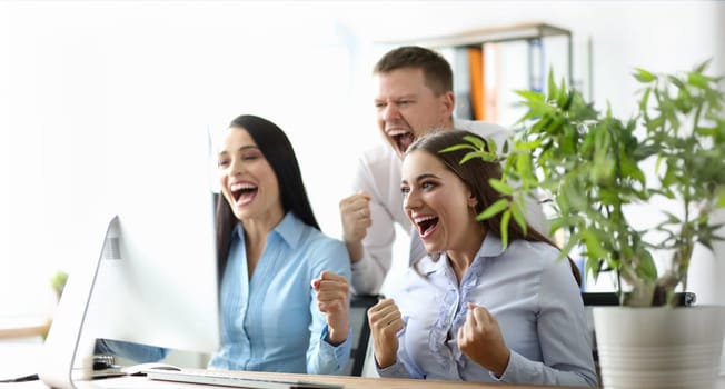 Portrait of beautiful businesspeople holding fists and shouting from happiness. Cheerful colleagues looking at laptop with gladness. Business company and teamwork concept
