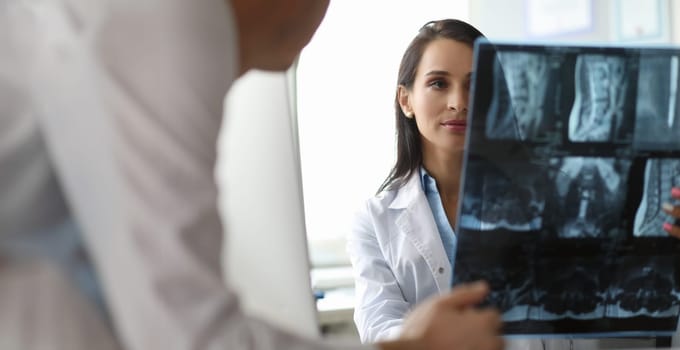 Portrait of serious surgeon looking carefully on spine x-ray in different projections. Cute doc discussing disease diagnosis with colleague. Healthcare concept