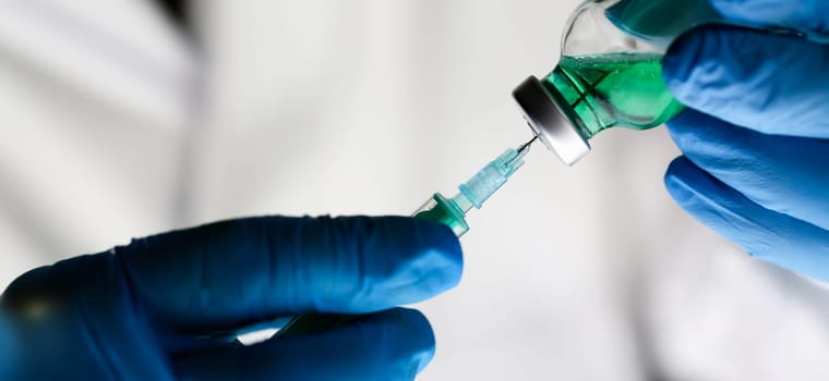 Physician injector arms in sterile uniform holding syringe while operating patient in surgical theatre closeup. HIV protection aids medication botulinum toxin innovation 911 team concept