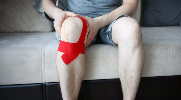 Male hands holding sored knee sitting on couch at home closeup
