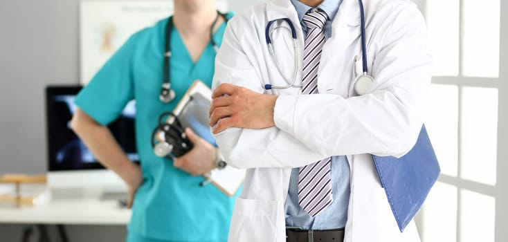 Male doctor with arms crossed on chest standing in line with colleagues in office closeup
