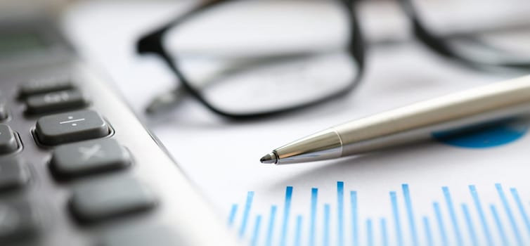 Silver pen gray calculator with paper chart and glasses lie in office table closeup. Business education concept