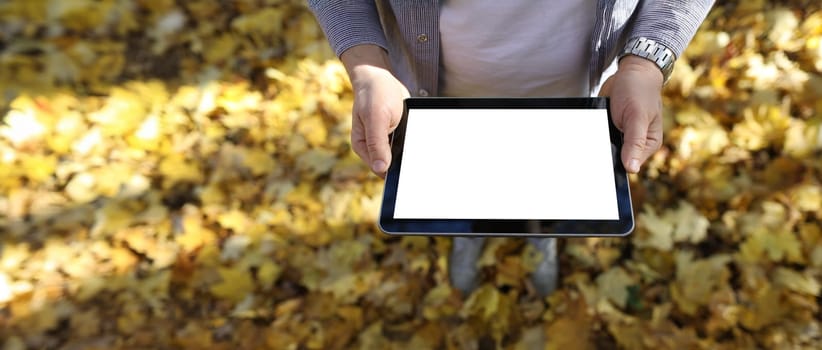 Man in pakr hold digital tablet pc with blank screen in park against yellow leaves background closeup. Autumn sales concept