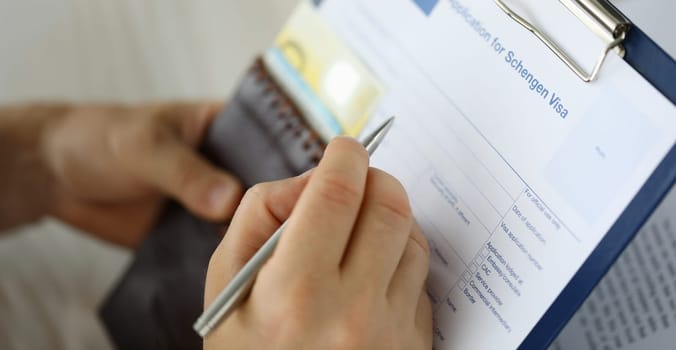 Focus on male hand writing answers to questions in questionnaire of application for schengen visa. Businessman holding paper folder. Travelling abroad or immigration concept. Blurred background