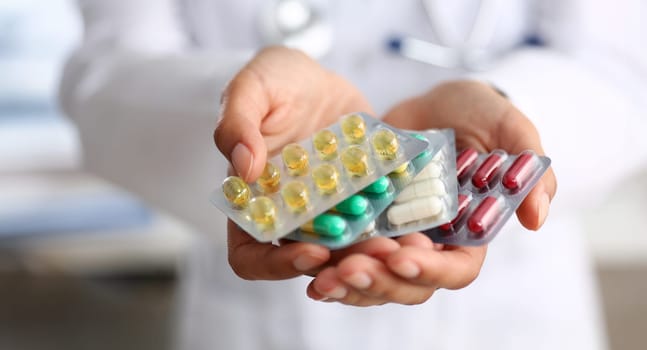 Female doctor hand holding pack of different tablet blisters at workplace closeup. Panacea life save service prescribe medicament legal drug store disease healing blood pressure concept