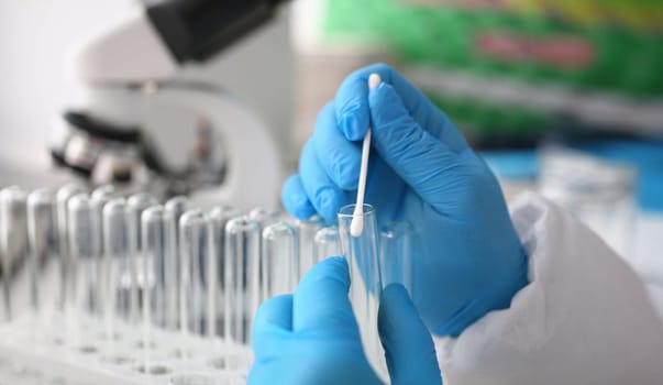 Forensic scientist conducting criminal investigation aganist laboratory background. Holds cotton swab with sample of dna and a test tube in his hand. Tets paternity concept.