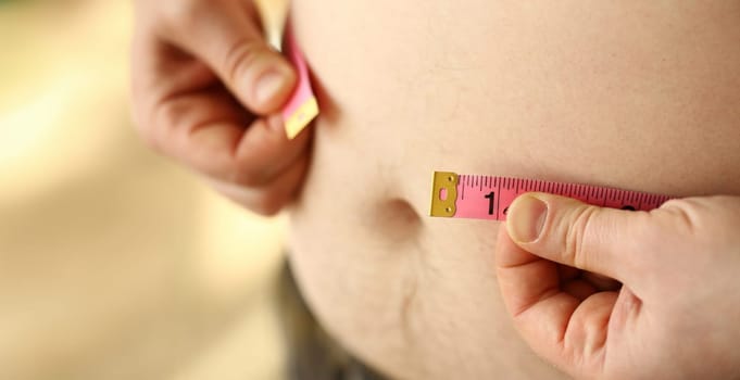 Thick man measuring belly with measuring tape. Concept of weight loss, dieting and healthy lifestyle. Figure of overweight person.