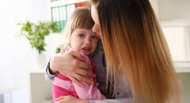 Doctor hugging scared crying little baby girl visiting her office portrait