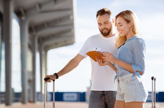 Traveling Together Concept. Two beautiful tourists looking at their documents standing ouside with luggage