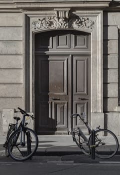 France, Paris - Jan 05, 2024 - Two bicycle parked at the side of the edge of road in front Traditional french building in downtown Paris. Brown wooden door entrance of old building with two Bicycle parked in front, Classical architecture of Antique building, Space for text, Selective focus.