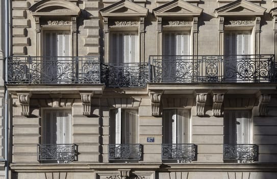 France, Paris - Jan 05, 2024 - Exterior architecture of Traditional French house with typical balconies and windows in Paris. Facade of elegant apartment buildings in the cities of Paris are patterned with french windows and wrought iron black railings, Space for text, Selective focus.