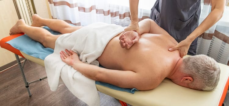 Female manual therapist performing physical therapy on mid aged male patient.