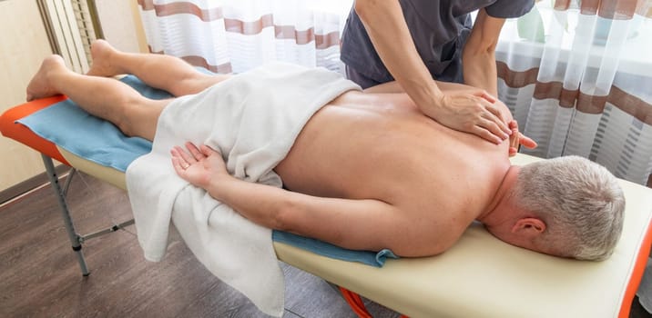 Female manual therapist performing physical therapy on mid aged male patient.