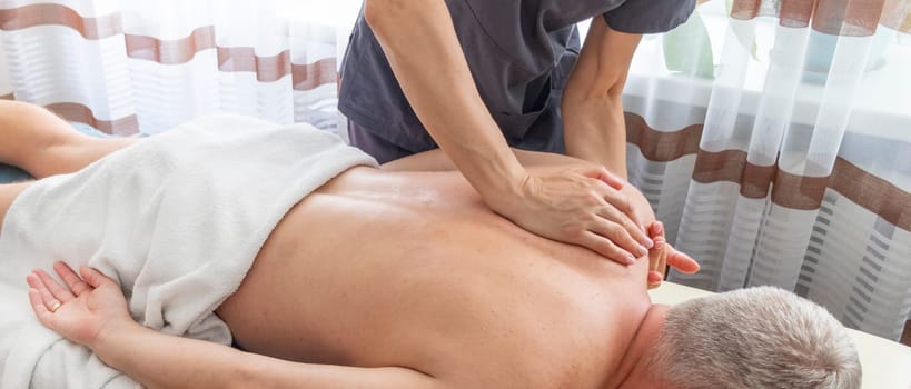 Female manual therapist performing physical therapy on mid aged male patient.
