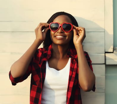 Summer portrait of pretty happy young african woman in red heart shaped glasses, beautiful girl smiling in sunglasses posing in the city