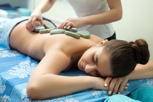 Young pretty girl lying on her stomach having stone massage in spa saloon