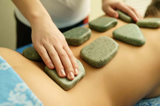 Young woman getting pleasure while lying on the stomach and receiving hot basalt stone massage in spa center. Beauty treatment concept, close-up, selective focus, shallow depth of field
