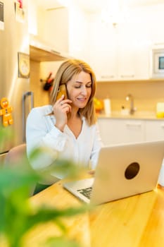 Vertical photo of a blonde businesswoman attending a call working from home sitting on a table next to the kitchen
