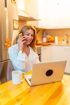 Vertical photo of a blonde caucasian adult businesswoman working from home in the morning using laptop and mobile phone next to coffee cup