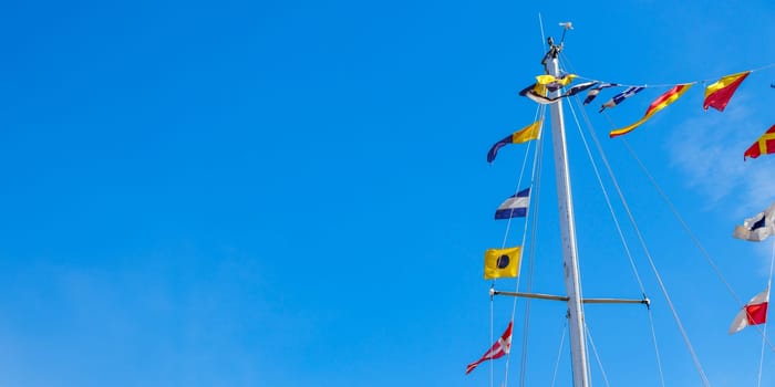 International maritime signal flags on a flagpole and masts on a sailing ship with a blue sky in the background. Banner