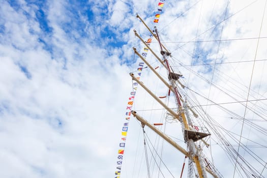 Sailing ship mast with flying nautical flags festival celebration decoration in a blue sunny sky and clouds, rigging of old tall ship with colorful bunting strung. Banner