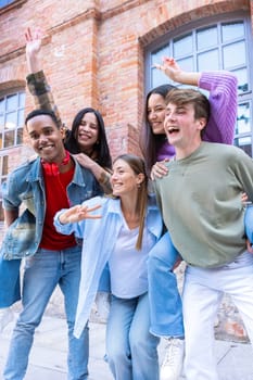 Young students having fun carrying their friends with their arms raised looking at the camera.Vertical