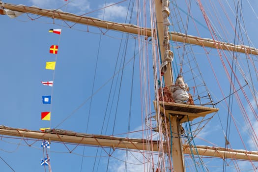 International maritime signal flags on a flagpole and masts on a sailing ship with a blue sky in the background. Banner