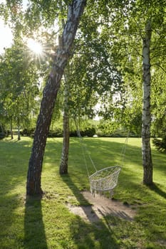 Bohemian style hammock hanging swing chair with tassels on ropes in a sunny summer or spring garden in beautiful sunlight