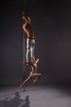 Athletic young male pole dancer making exercises in pair with little girl in studio