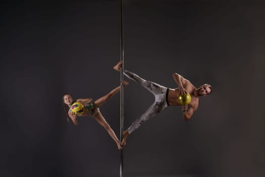 Athletic young male pole dancer in sports trousers making exercises in pair with little girl - studio shot