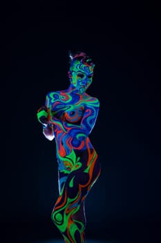 Slim girl posing in smoky studio her face and figure covered by bright fantastic ultraviolet color pattern bodyart.