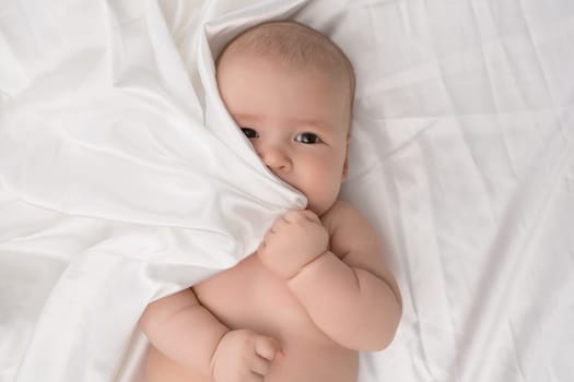 Baby boy lying on white linen looking attentively close up studio shot from above