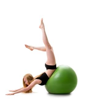 Long haired blonde in black shorts and briefs lying on her stomack on green big fitball posing in studio with her legs streching up