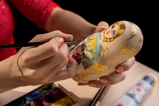 Pretty woman drawing patterns with a brush on russian folk toy matrioshka studio shot