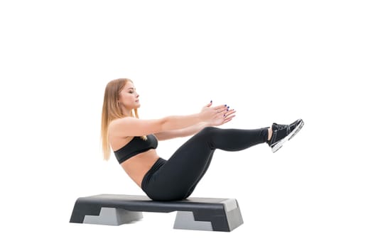 Pretty fitness trainer in black top and leggings exercising on step platform in studio isolated photo