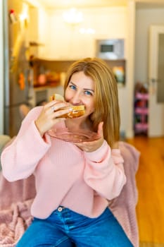 Vertical portrait of a hungry woman biting a home made healthy sandwich sitting on the sofa at home